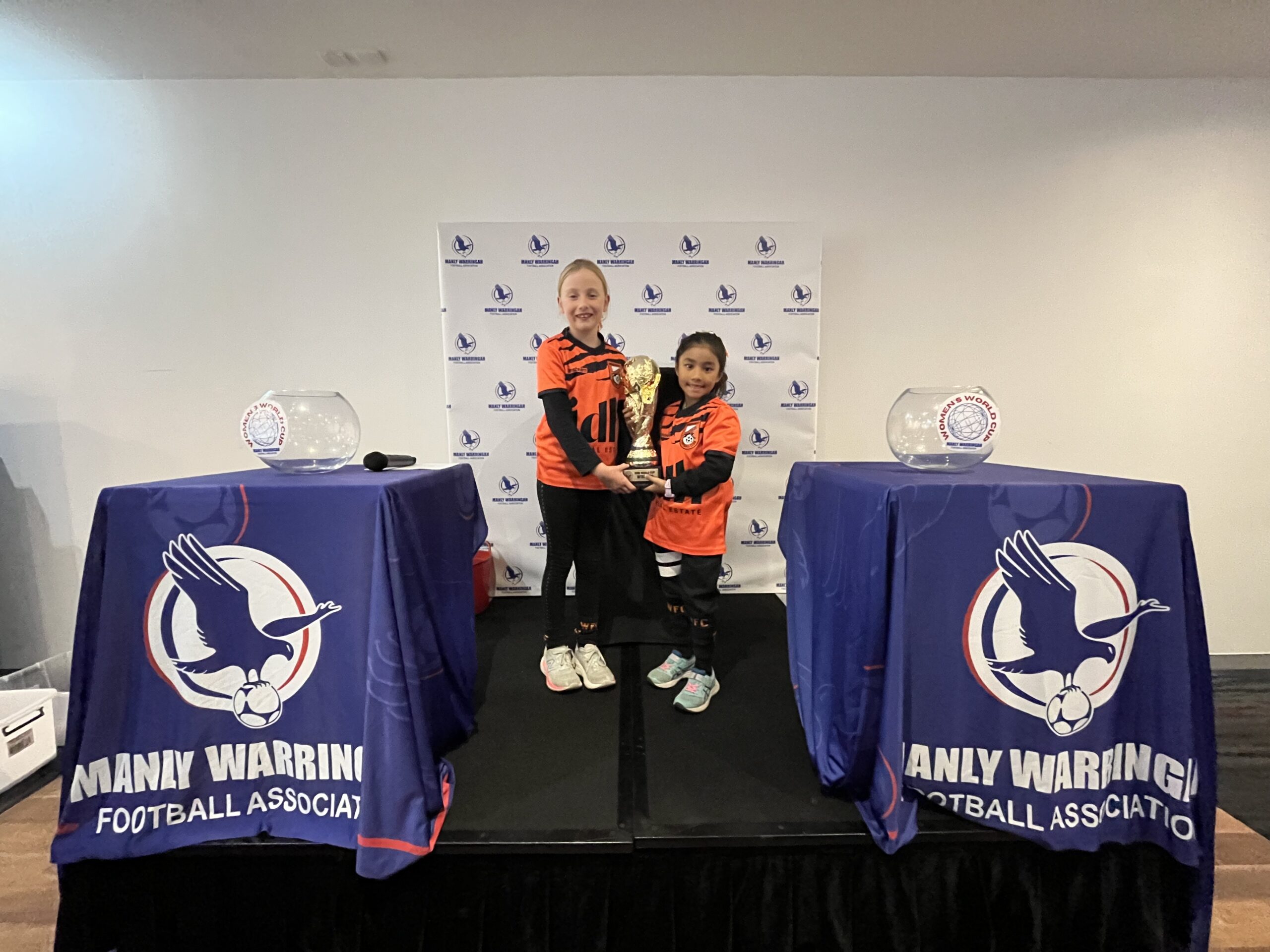 Two Wakehurst juniors pose with the trophy at the draw ceremony for the 2023 MWFA Women's World Cup.