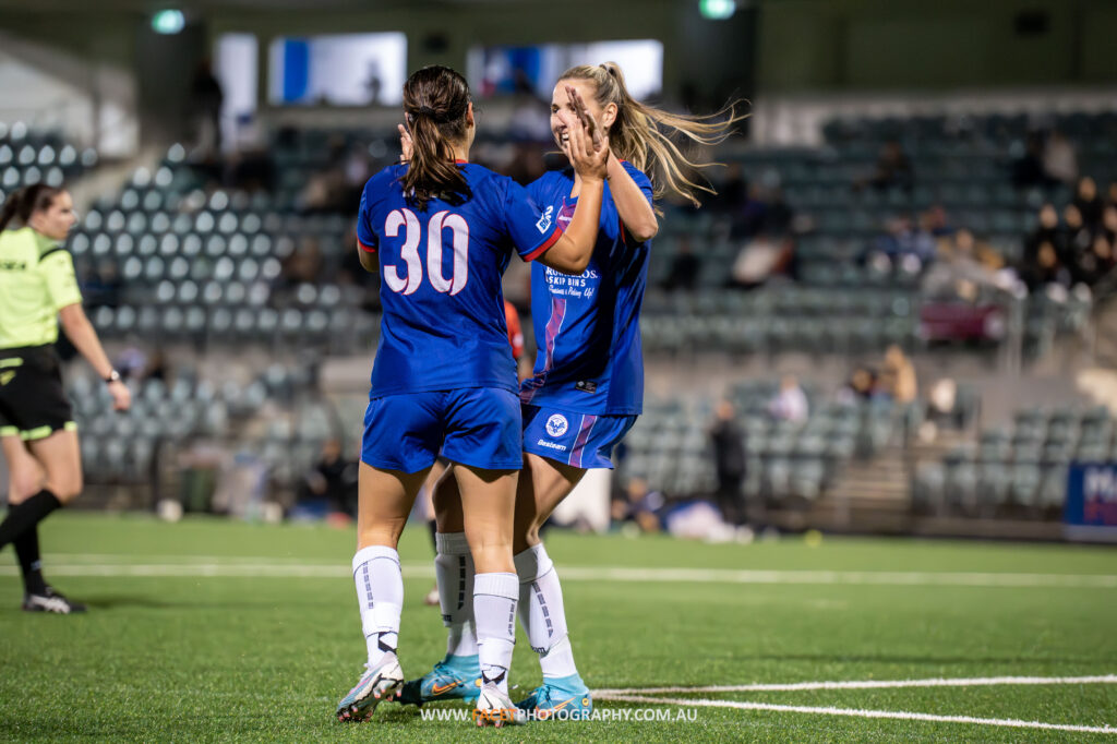 Wakehurst juniors Sienna Dale and Emily Minett celebrate a goal during the 2023 NPL NSW Women's Round 12 game between Manly United and Bankstown City. Photo credit: Jeremy Denham
